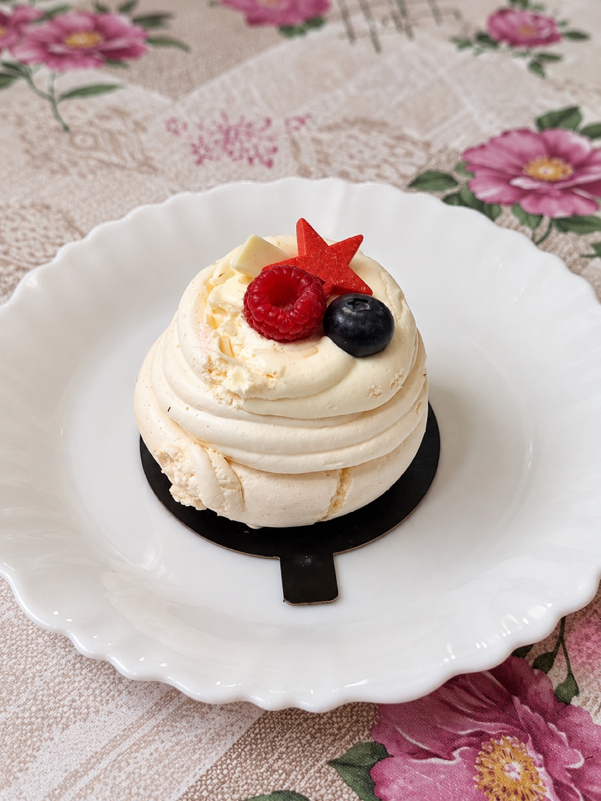 Une meringue couronnée de crème, d'une framboise et d'une myrtille, sur une assiette festonnée